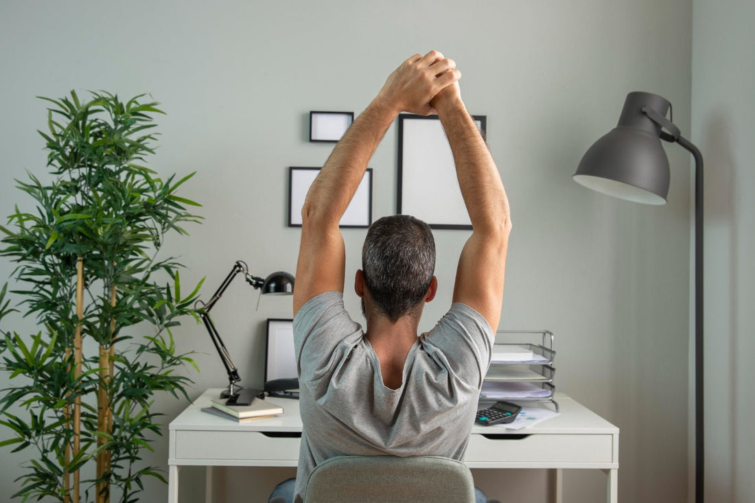 Back view of man at desk stretching while working from home