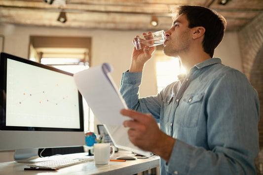 Young man having a glass of water while working on paperwork in the office