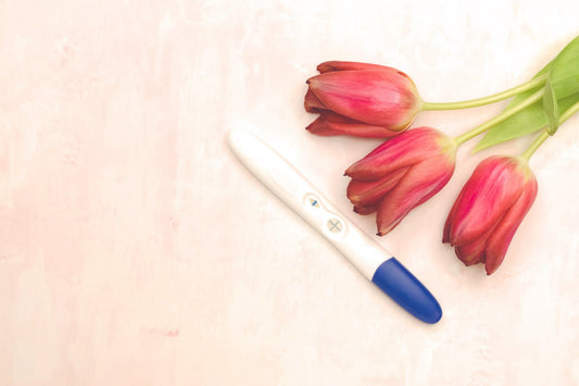 A positive pregnancy test with red tulips on pink background