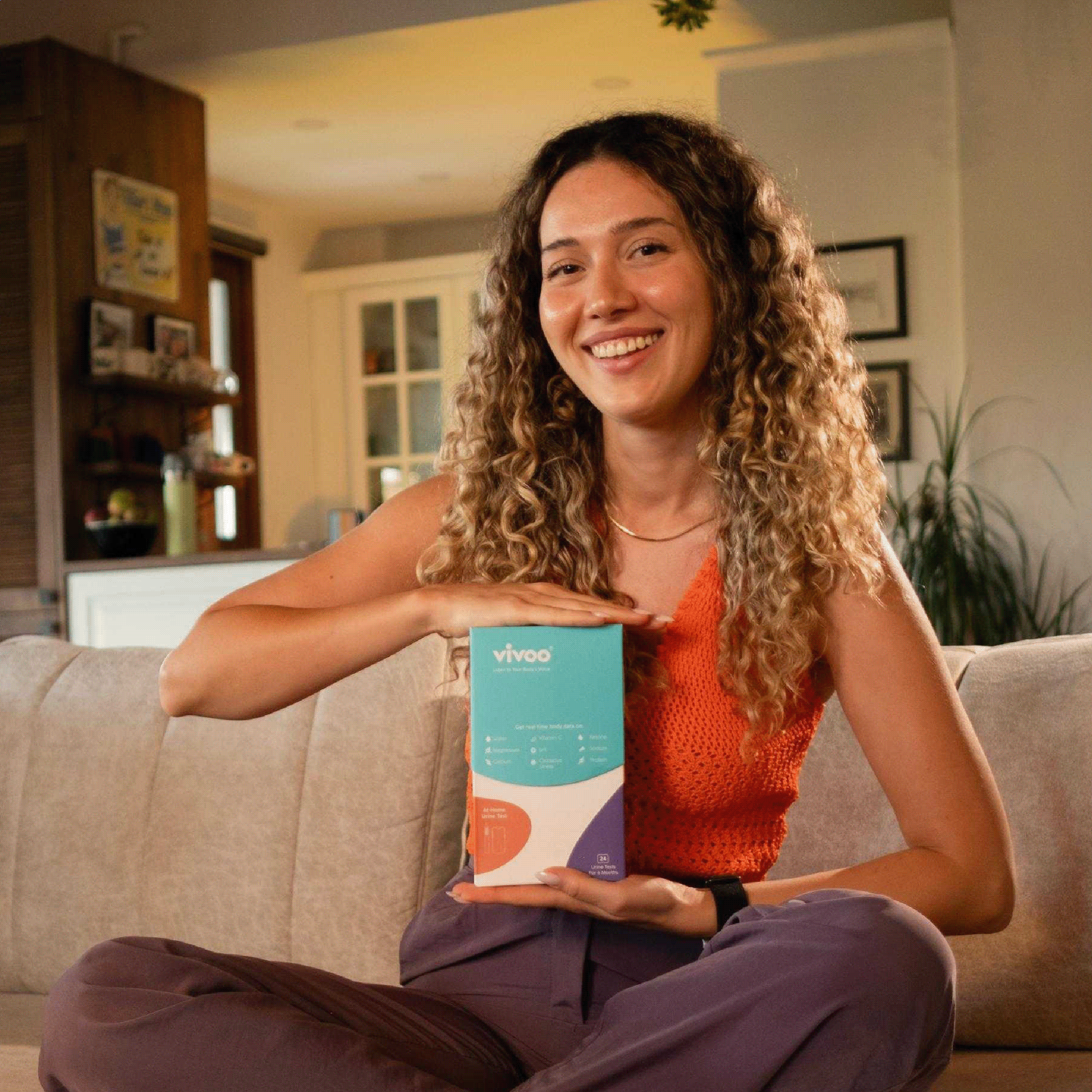 Woman sitting on a couch holding a Vivoo box in a living room.