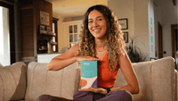 Woman holding a box with a brand logo on a couch in a living room.