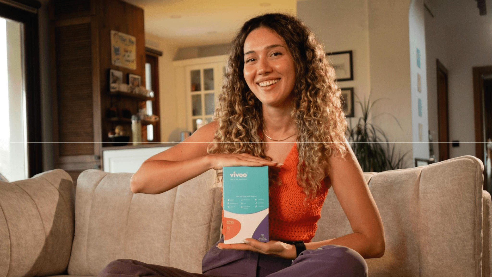 Woman holding a box with a brand logo on a couch in a living room.